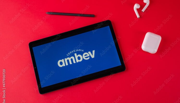 Tablet com logo da Ambev. Imagem de tablet com o logo da Ambev, fones de ouvido e caneta sobre fundo vermelho.
