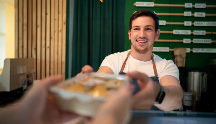 McDonald’s anuncia vagas para Atendente e Auxiliar de Limpeza Atendente de restaurante sorrindo enquanto entrega um pedido, ilustrando as oportunidades de emprego para Atendente e Auxiliar de Limpeza no McDonald’s.