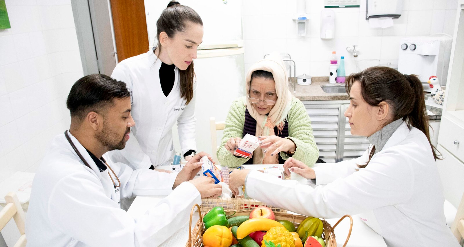 Alunos de Enfermagem da Unoeste durante aula prática em ambiente de Casa Simulada, realizando atividade de visita domiciliar com paciente idosa, orientando sobre o uso de medicamentos e hábitos saudáveis.