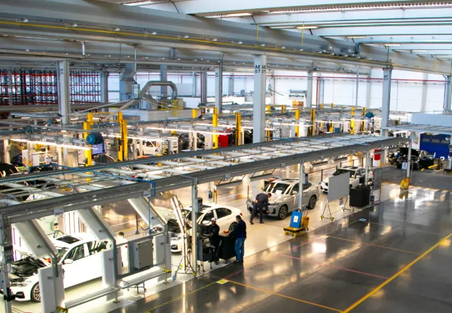 Novas vagas de emprego na BMW Group Brasil na linha de montagem. Linha de produção da BMW Group Brasil com carros sendo montados e funcionários trabalhando.