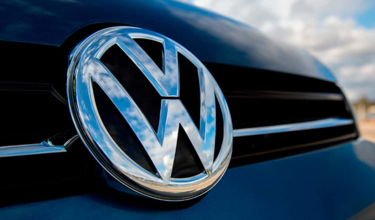 Emblema Volkswagen brilhando na frente de um carro azul, simbolizando oportunidades de emprego na empresa.