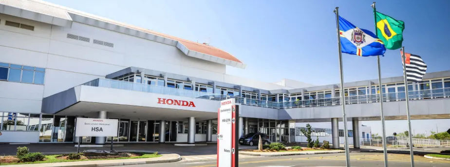 Honda anuncia expansão de vagas no Brasil. Fachada da unidade Honda com bandeiras do Brasil e do estado ao lado, simbolizando expansão da empresa.